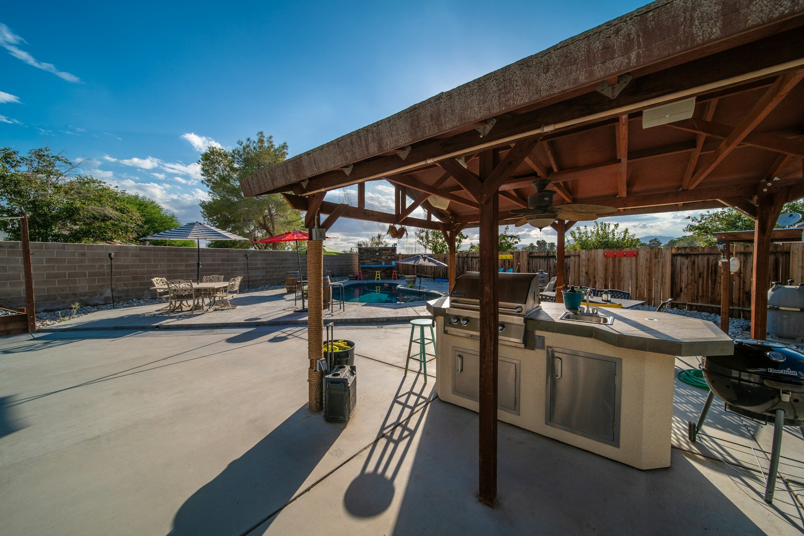 A wood-roofed covered patio with an outdoor kitchen, open to a sunny backyard.