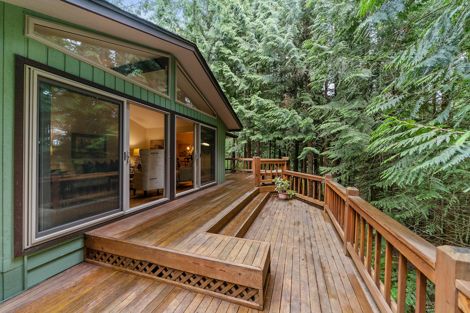 A finished wood deck wrapping a home, surrounded by tall trees.