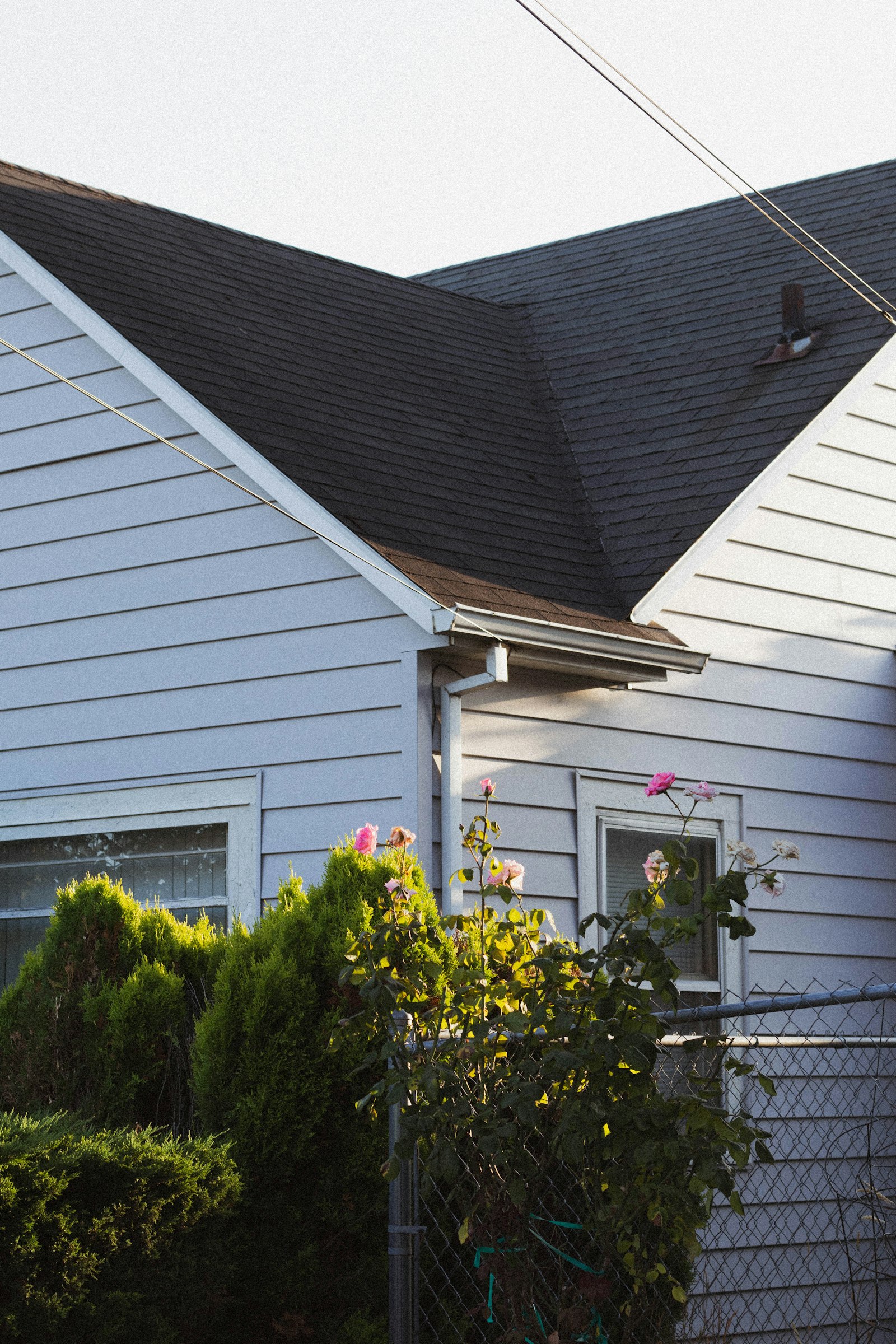 A close view of a home roof with dark asphalt shingles meeting two siding gables.